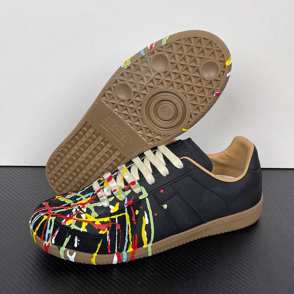 Maison Margiela Replica low-top sneaker in matte black calfskin leather featuring an avant-garde multicolor hand-splattered paint drop design across the toe box and a classic gum sole, style code S58WS0109P1895T1016.