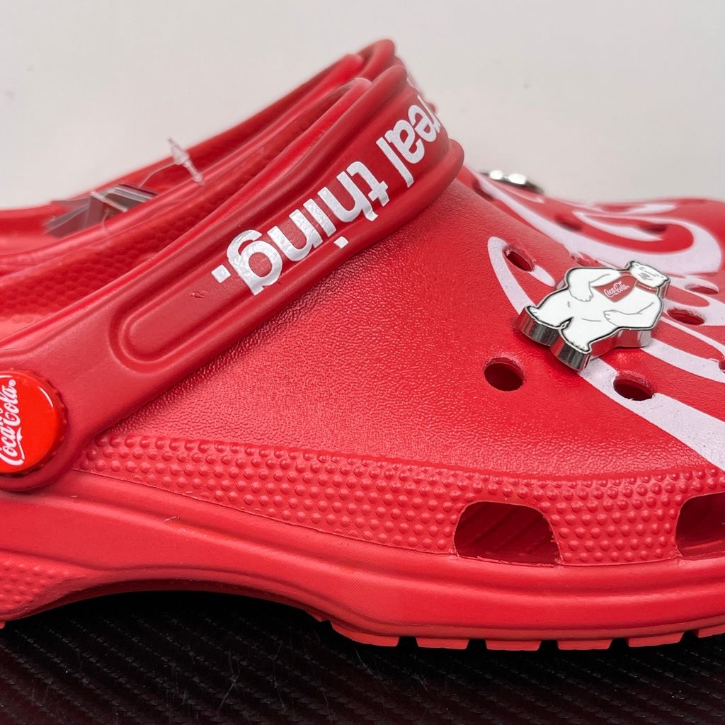 Side profile of the red Crocs x Coca-Cola Classic Clog featuring a Polar Bear Jibbitz charm, a white Coca-Cola script graphic, and red Coca-Cola logo rivets.