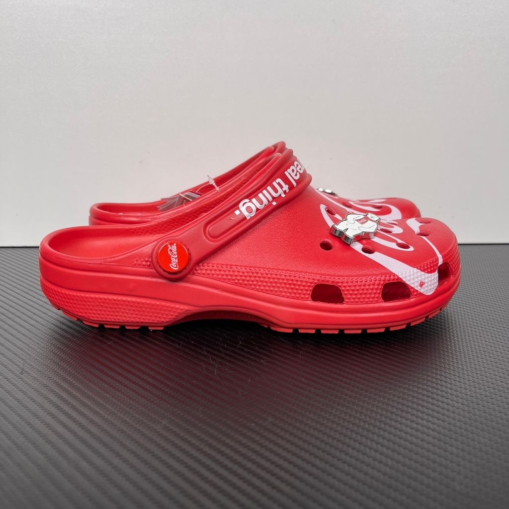 Side profile of the red Crocs x Coca-Cola Classic Clog featuring a Polar Bear Jibbitz charm, a white Coca-Cola script graphic, and red Coca-Cola logo rivets.