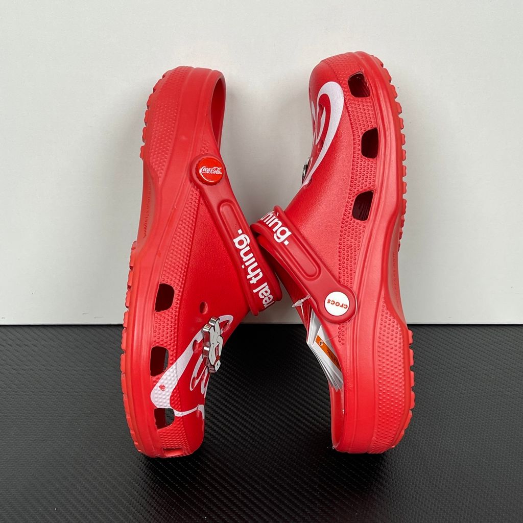 Side profile of the red Crocs x Coca-Cola Classic Clog featuring a Polar Bear Jibbitz charm, a white Coca-Cola script graphic, and red Coca-Cola logo rivets.