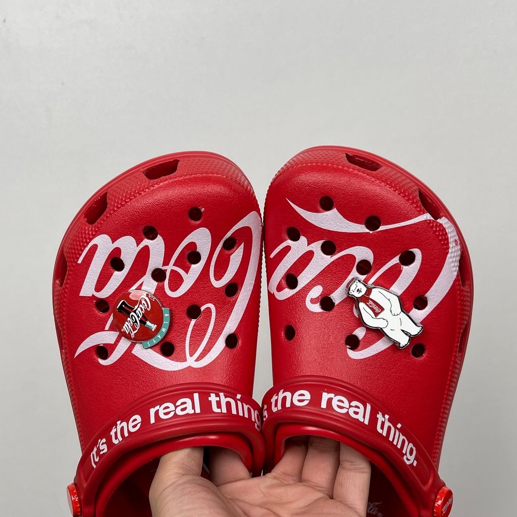 Side profile of the red Crocs x Coca-Cola Classic Clog featuring a Polar Bear Jibbitz charm, a white Coca-Cola script graphic, and red Coca-Cola logo rivets.