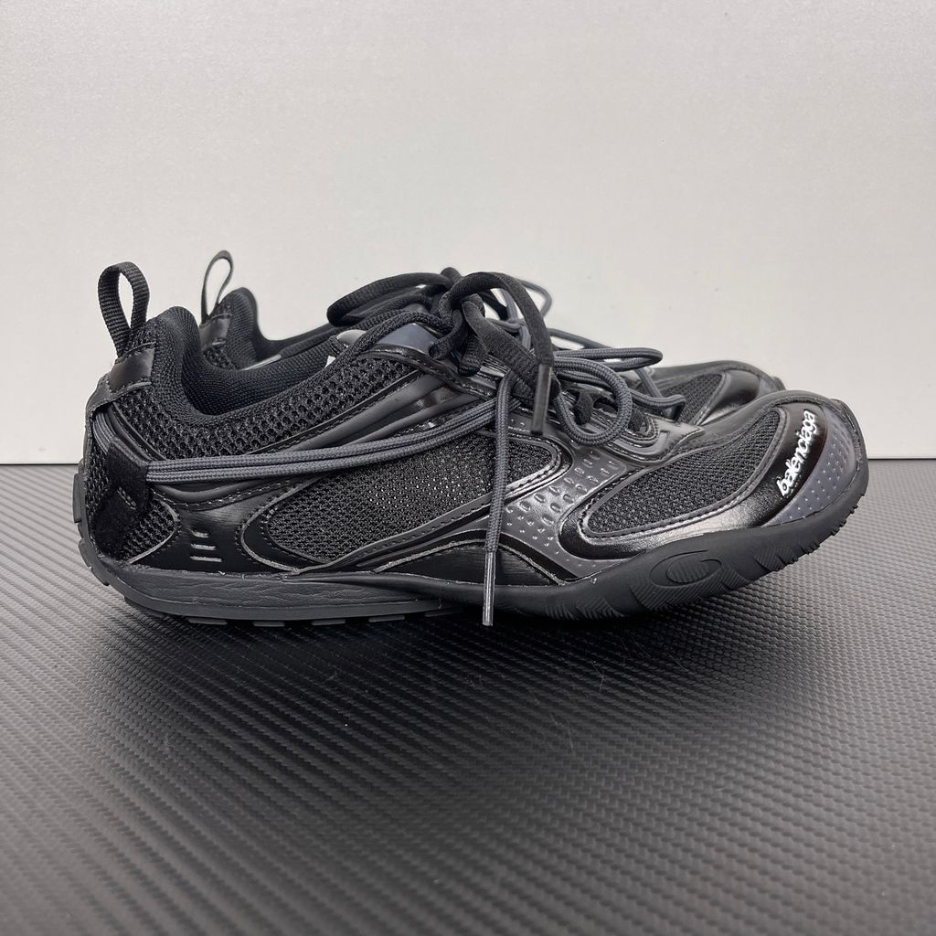 Balenciaga Radar low-profile sneaker in all black, featuring breathable mesh panels, sleek synthetic overlays, a thin driving-style sole, and the classic white Balenciaga logo on the toe edge, SKU 865704WSTE1011.