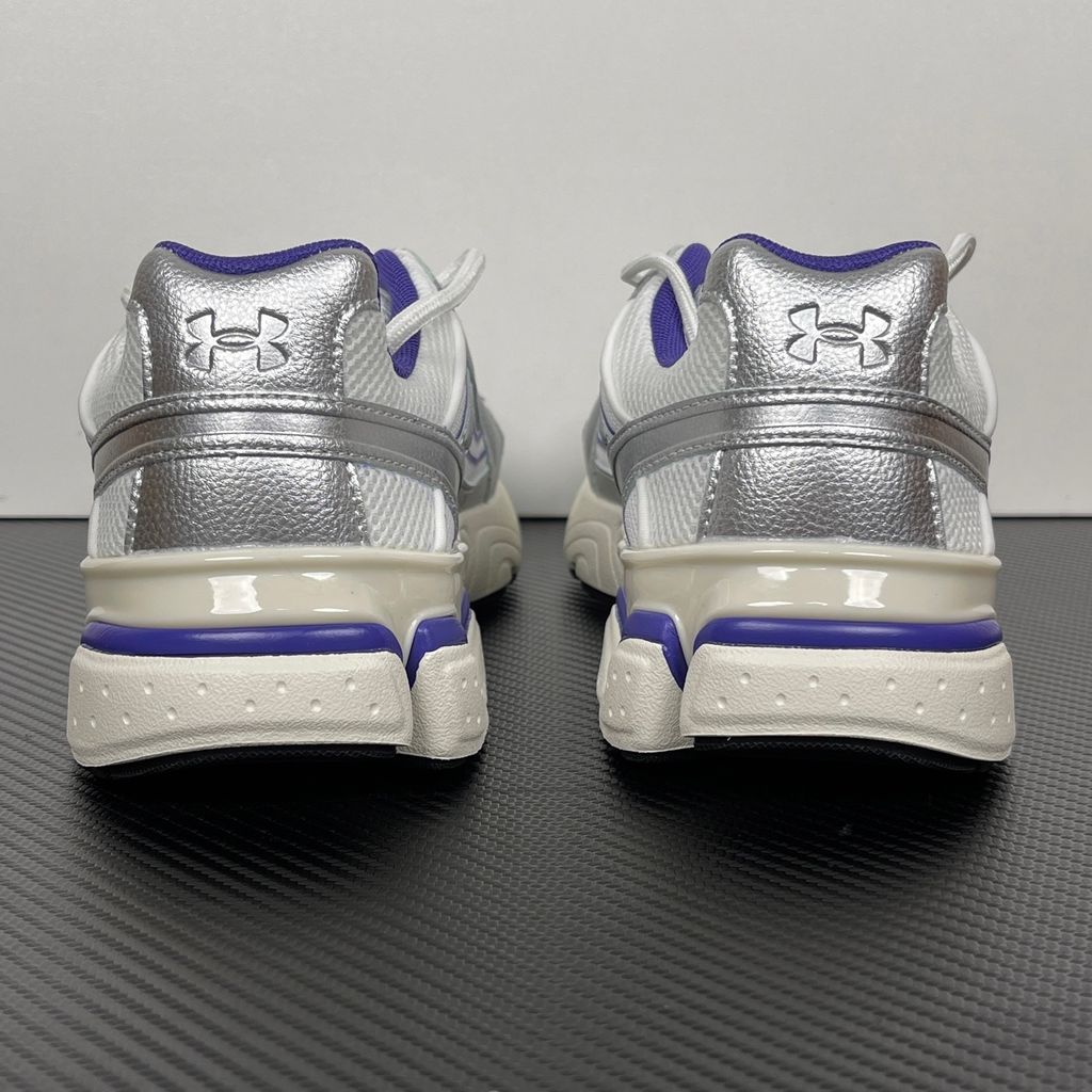 Under Armour UA Sola retro tech-runner side profile, featuring a white breathable mesh upper, dynamic metallic silver synthetic overlays, and vibrant purple accents on the midsole and collar, SKU 6005284-103.