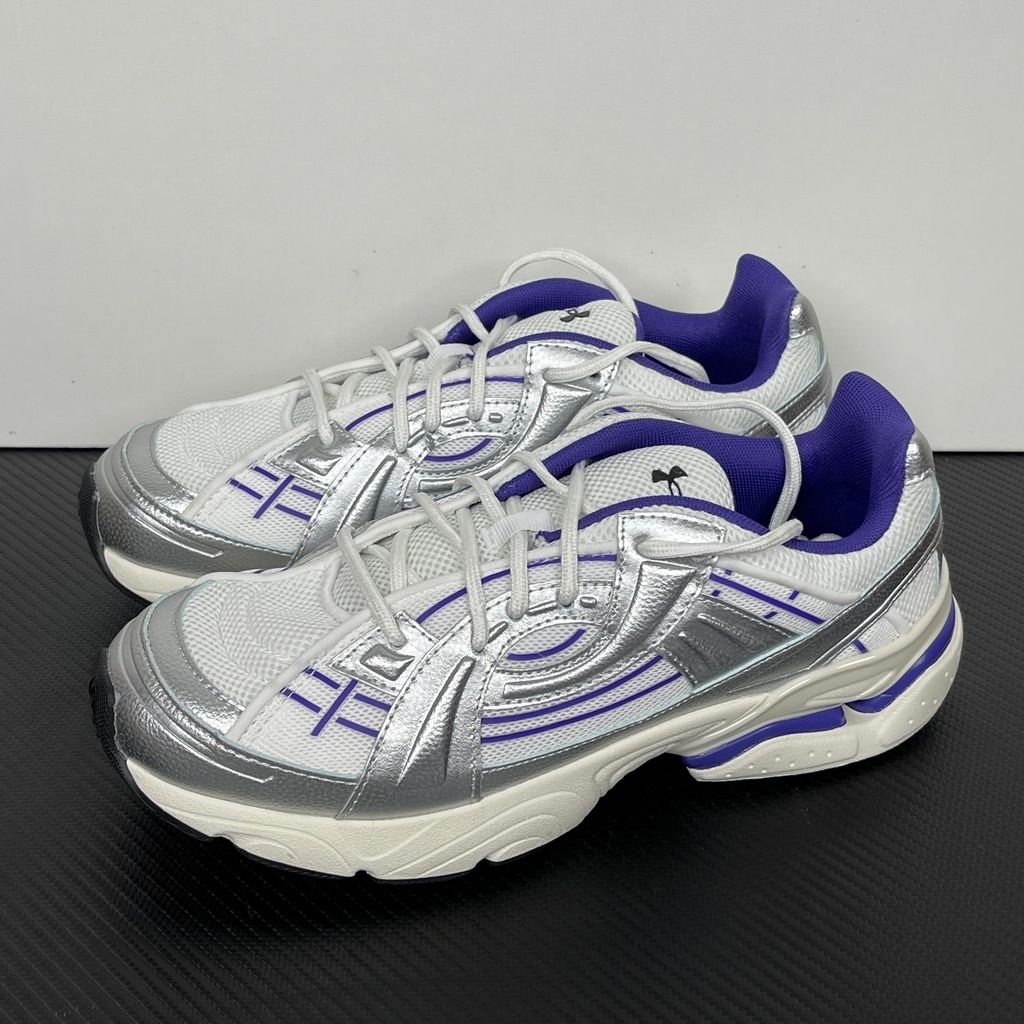 Under Armour UA Sola retro tech-runner side profile, featuring a white breathable mesh upper, dynamic metallic silver synthetic overlays, and vibrant purple accents on the midsole and collar, SKU 6005284-103.