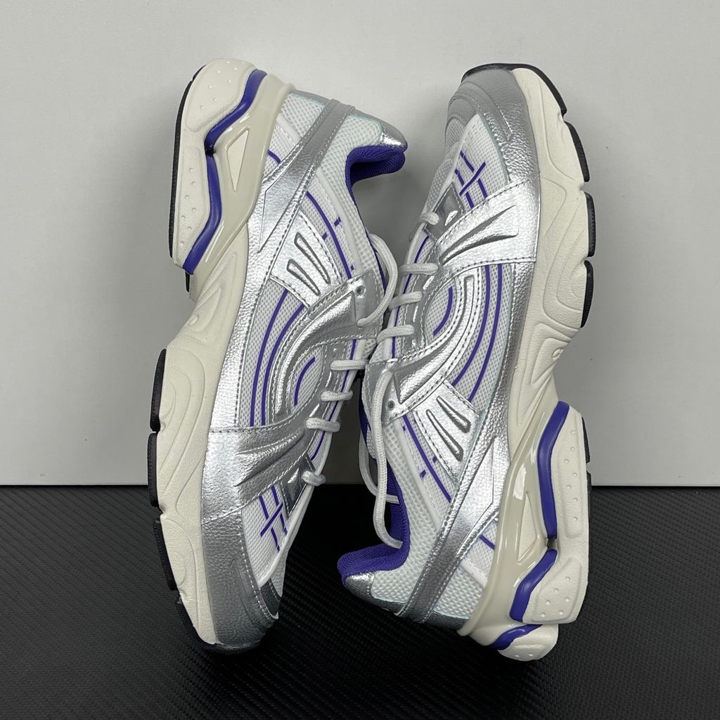 Under Armour UA Sola retro tech-runner side profile, featuring a white breathable mesh upper, dynamic metallic silver synthetic overlays, and vibrant purple accents on the midsole and collar, SKU 6005284-103.