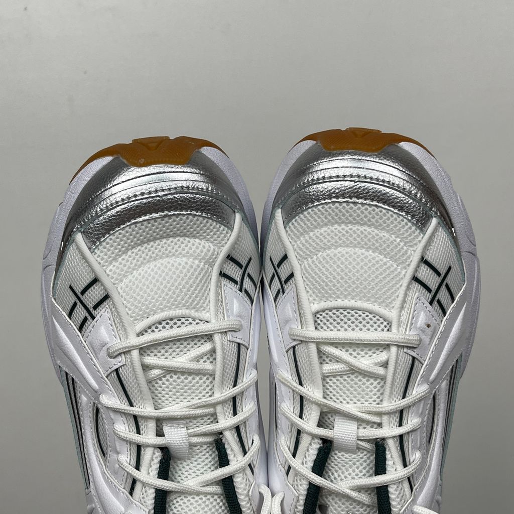 Under Armour UA Sola retro tech-runner side profile, featuring a clean white breathable mesh upper, dynamic metallic silver overlays, dark green collar lining, bright yellow midsole accents, and a classic gum rubber outsole, SKU 6005284-104.