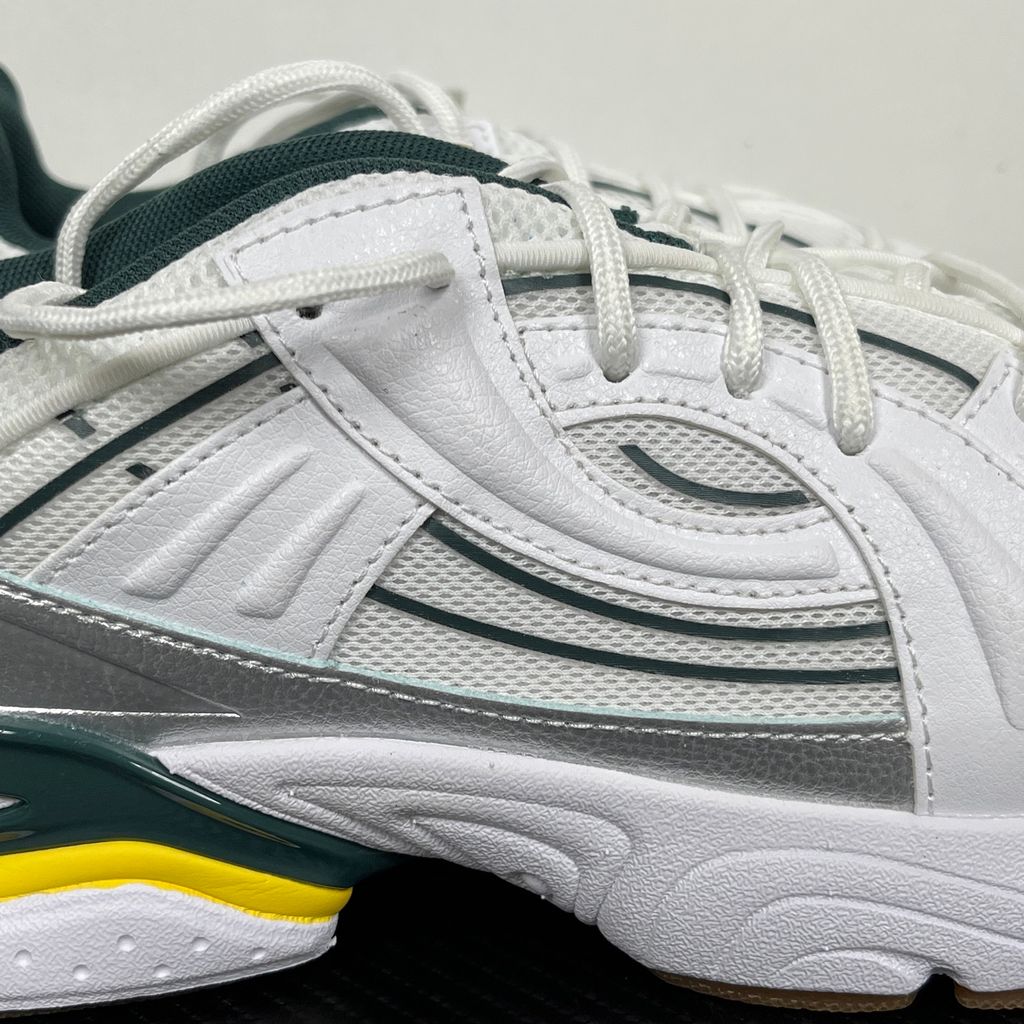 Under Armour UA Sola retro tech-runner side profile, featuring a clean white breathable mesh upper, dynamic metallic silver overlays, dark green collar lining, bright yellow midsole accents, and a classic gum rubber outsole, SKU 6005284-104.