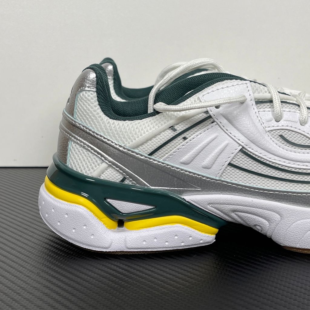 Under Armour UA Sola retro tech-runner side profile, featuring a clean white breathable mesh upper, dynamic metallic silver overlays, dark green collar lining, bright yellow midsole accents, and a classic gum rubber outsole, SKU 6005284-104.