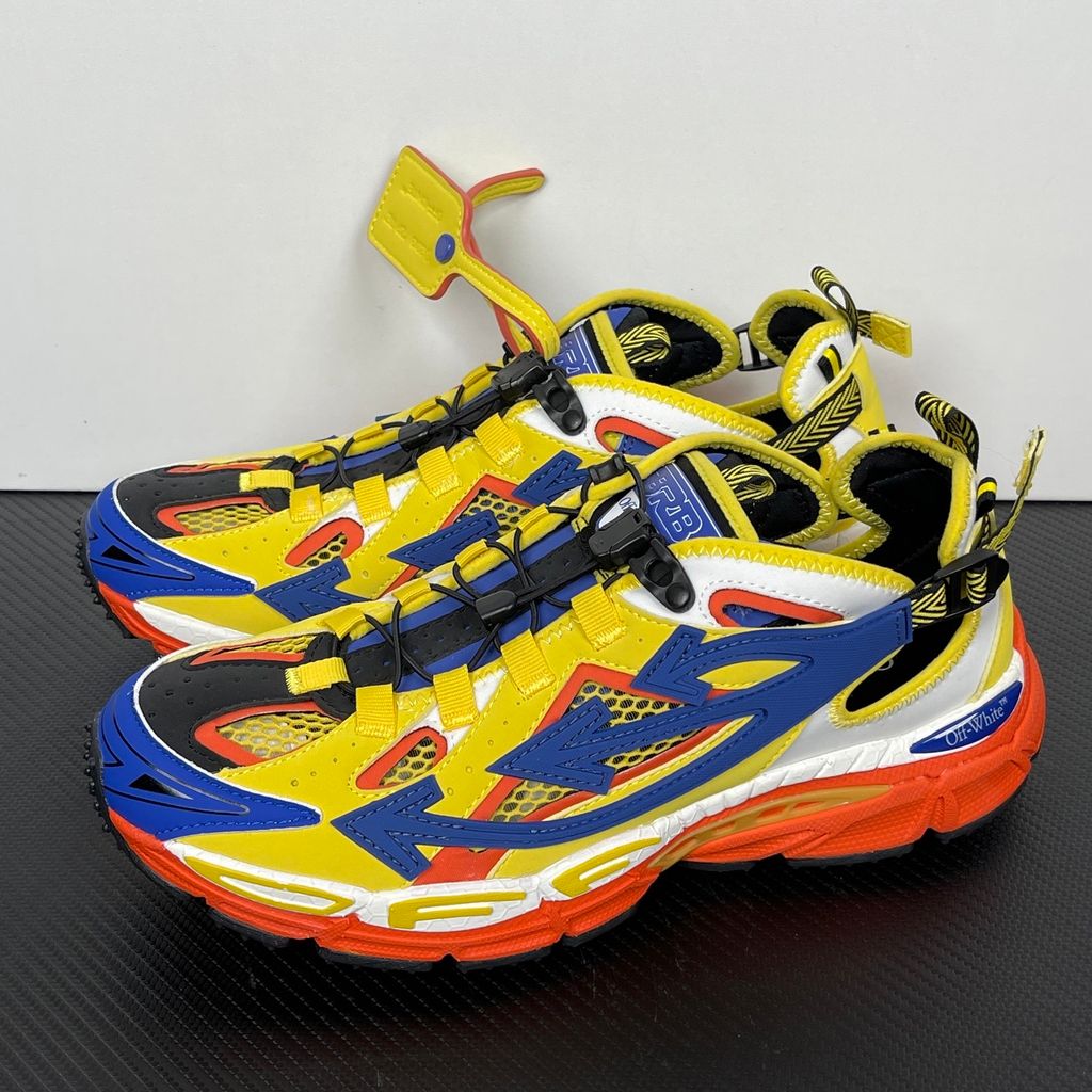 Side profile of the Off-White "Be Right" sneaker featuring a vibrant yellow mesh upper, bold blue signature arrow overlays, a chunky orange sculpted midsole, and black technical heel straps.