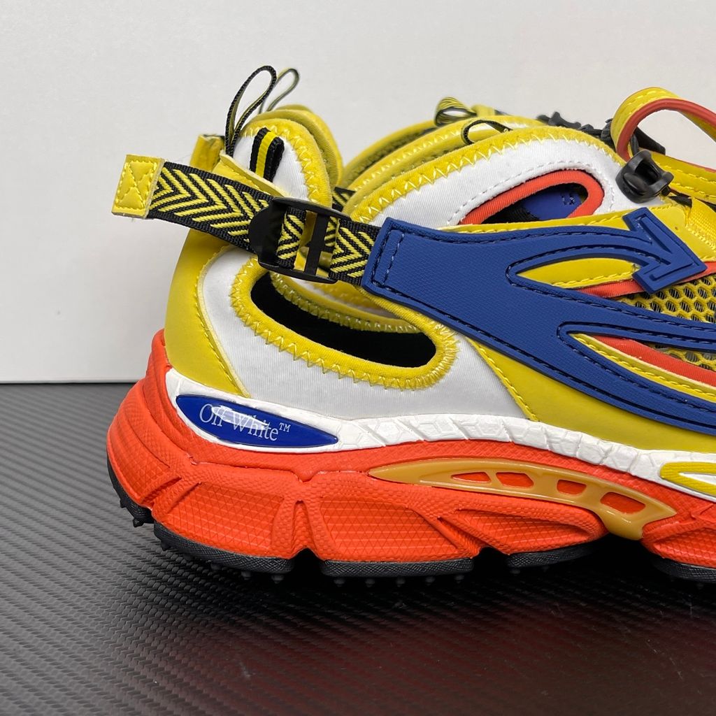Side profile of the Off-White "Be Right" sneaker featuring a vibrant yellow mesh upper, bold blue signature arrow overlays, a chunky orange sculpted midsole, and black technical heel straps.