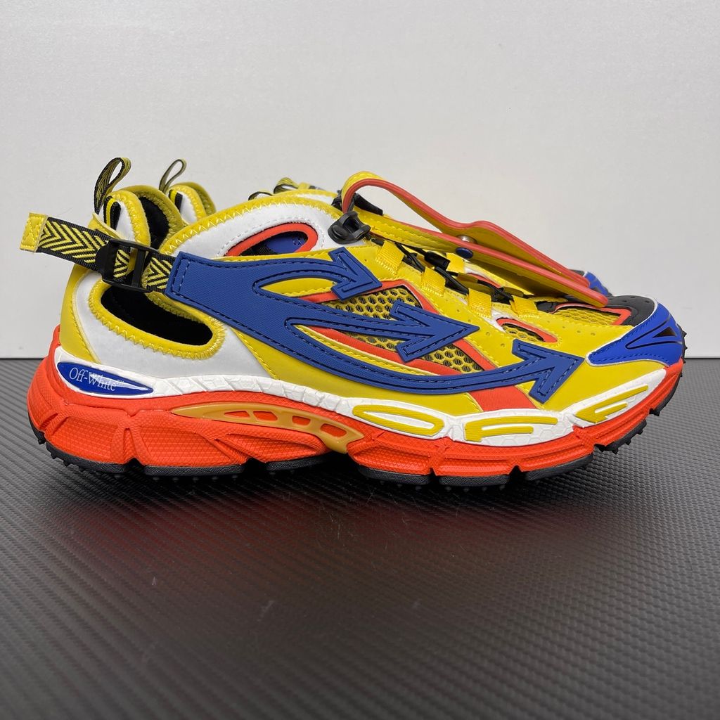 Side profile of the Off-White "Be Right" sneaker featuring a vibrant yellow mesh upper, bold blue signature arrow overlays, a chunky orange sculpted midsole, and black technical heel straps.