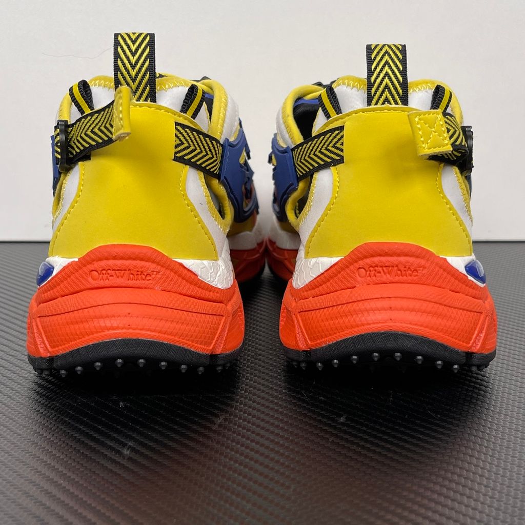 Side profile of the Off-White "Be Right" sneaker featuring a vibrant yellow mesh upper, bold blue signature arrow overlays, a chunky orange sculpted midsole, and black technical heel straps.