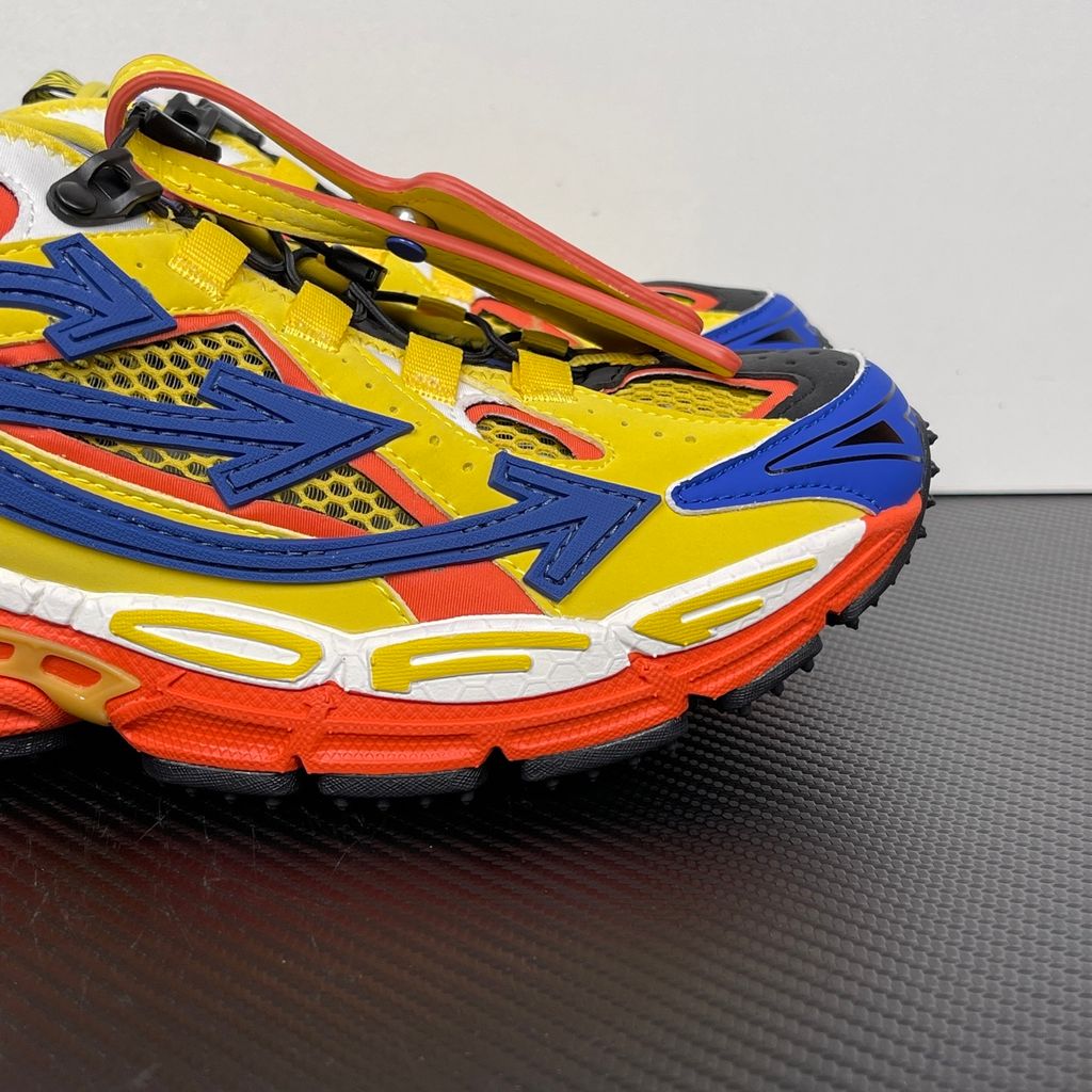 Side profile of the Off-White "Be Right" sneaker featuring a vibrant yellow mesh upper, bold blue signature arrow overlays, a chunky orange sculpted midsole, and black technical heel straps.
