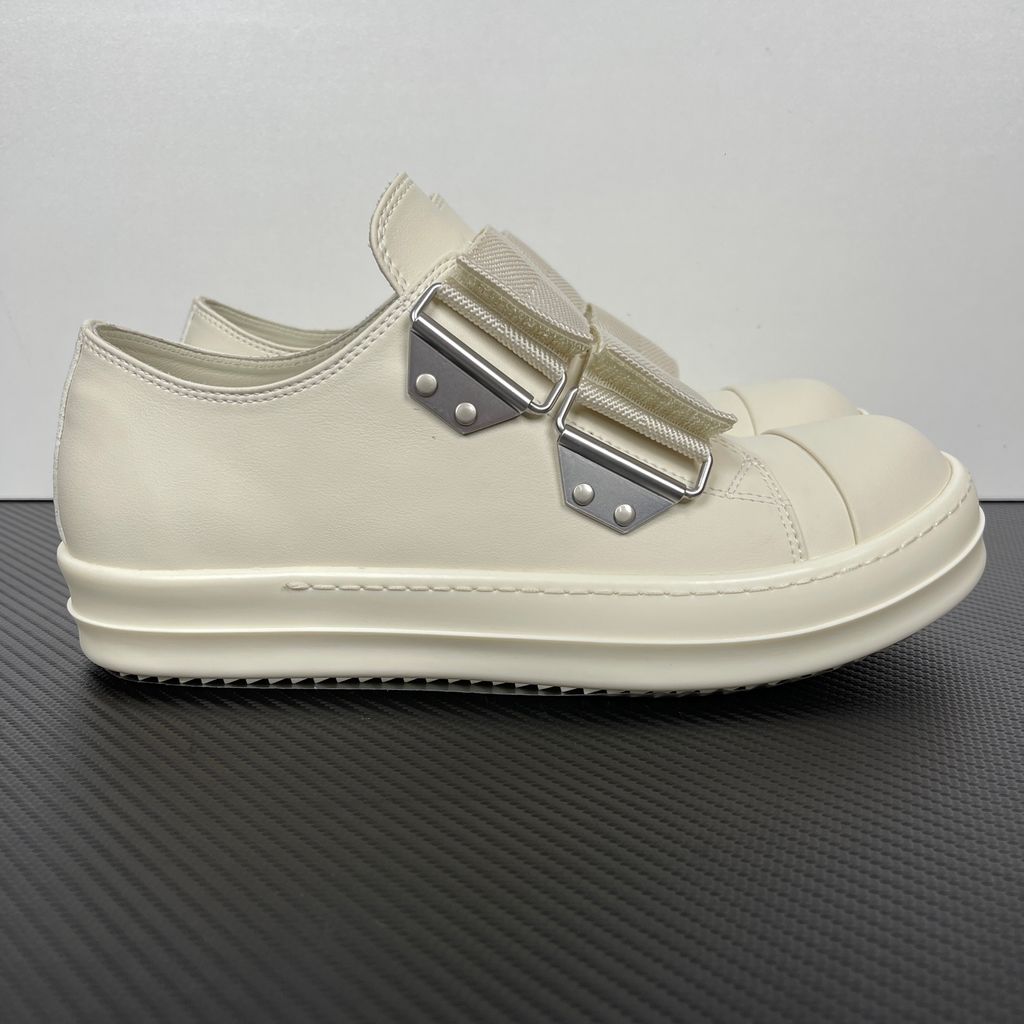 Side profile of the Rick Owens Mainline low-top sneaker in off-white leather, featuring distinctive industrial metal hardware, textured velcro strap closures, and a chunky tonal rubber sole.