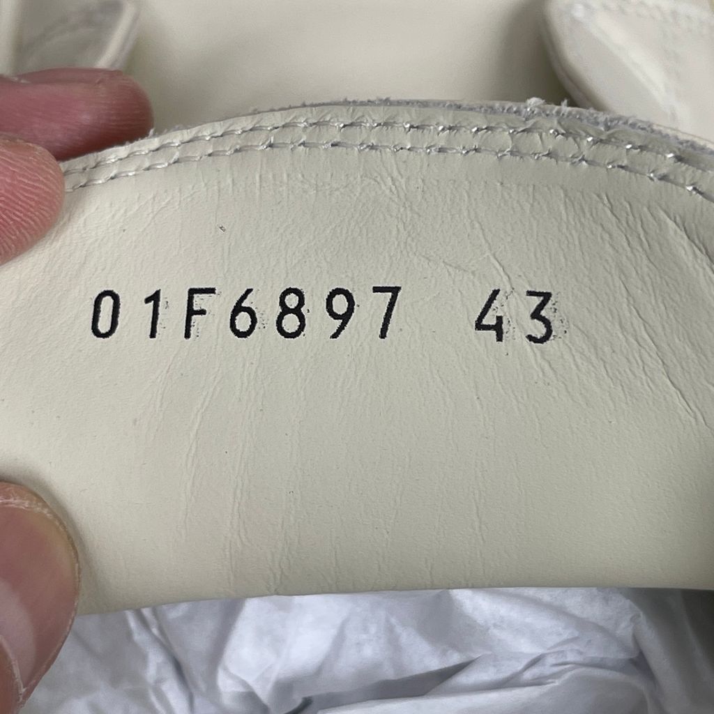 Side profile of the Rick Owens Mainline low-top sneaker in off-white leather, featuring distinctive industrial metal hardware, textured velcro strap closures, and a chunky tonal rubber sole.