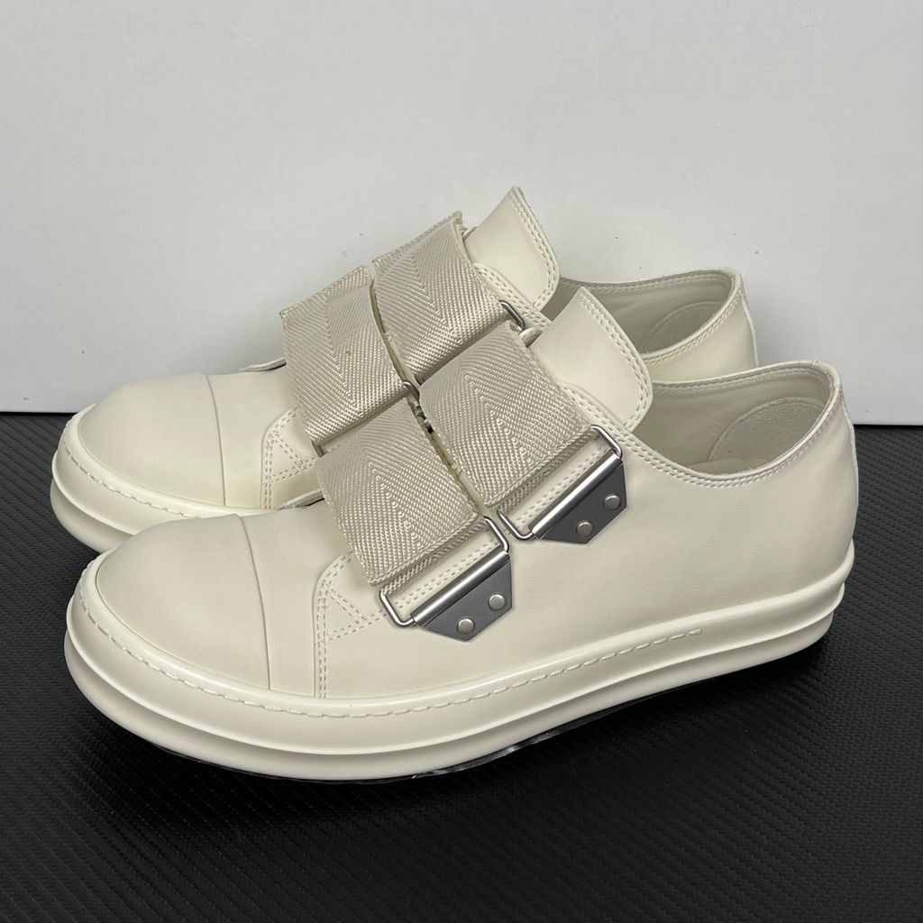 Side profile of the Rick Owens Mainline low-top sneaker in off-white leather, featuring distinctive industrial metal hardware, textured velcro strap closures, and a chunky tonal rubber sole.