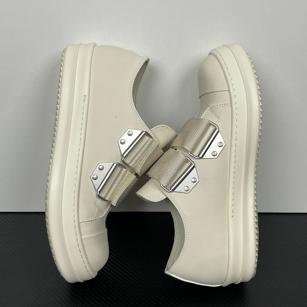 Side profile of the Rick Owens Mainline low-top sneaker in off-white leather, featuring distinctive industrial metal hardware, textured velcro strap closures, and a chunky tonal rubber sole.