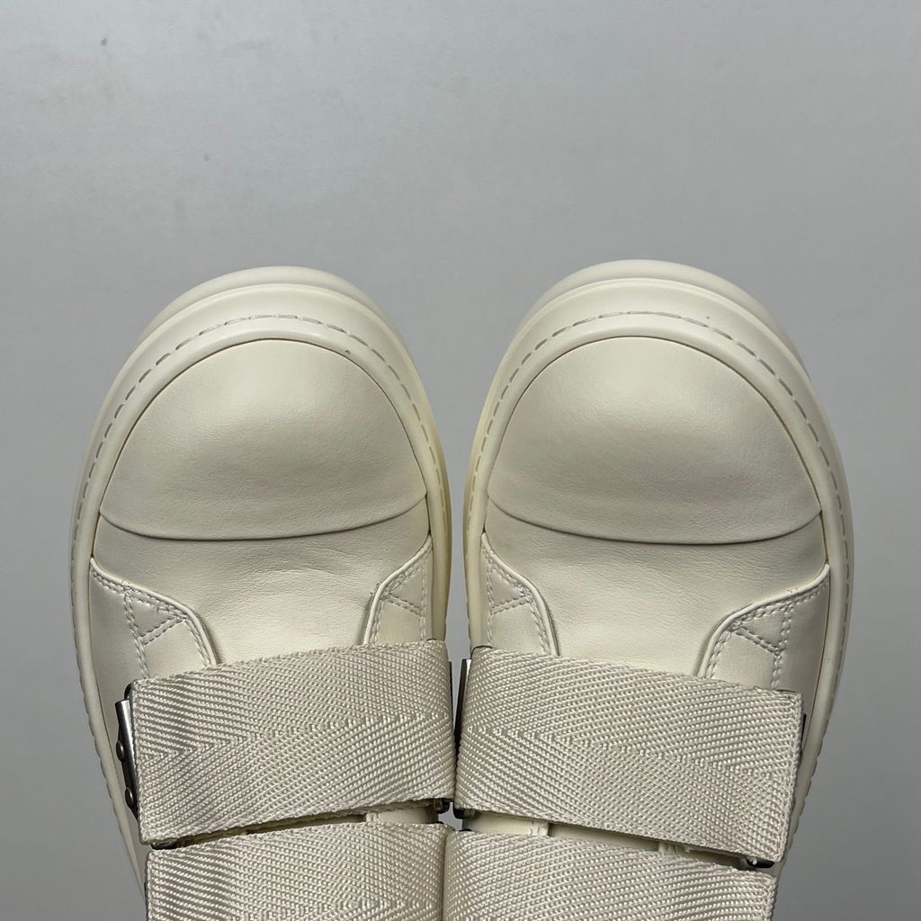 Side profile of the Rick Owens Mainline low-top sneaker in off-white leather, featuring distinctive industrial metal hardware, textured velcro strap closures, and a chunky tonal rubber sole.