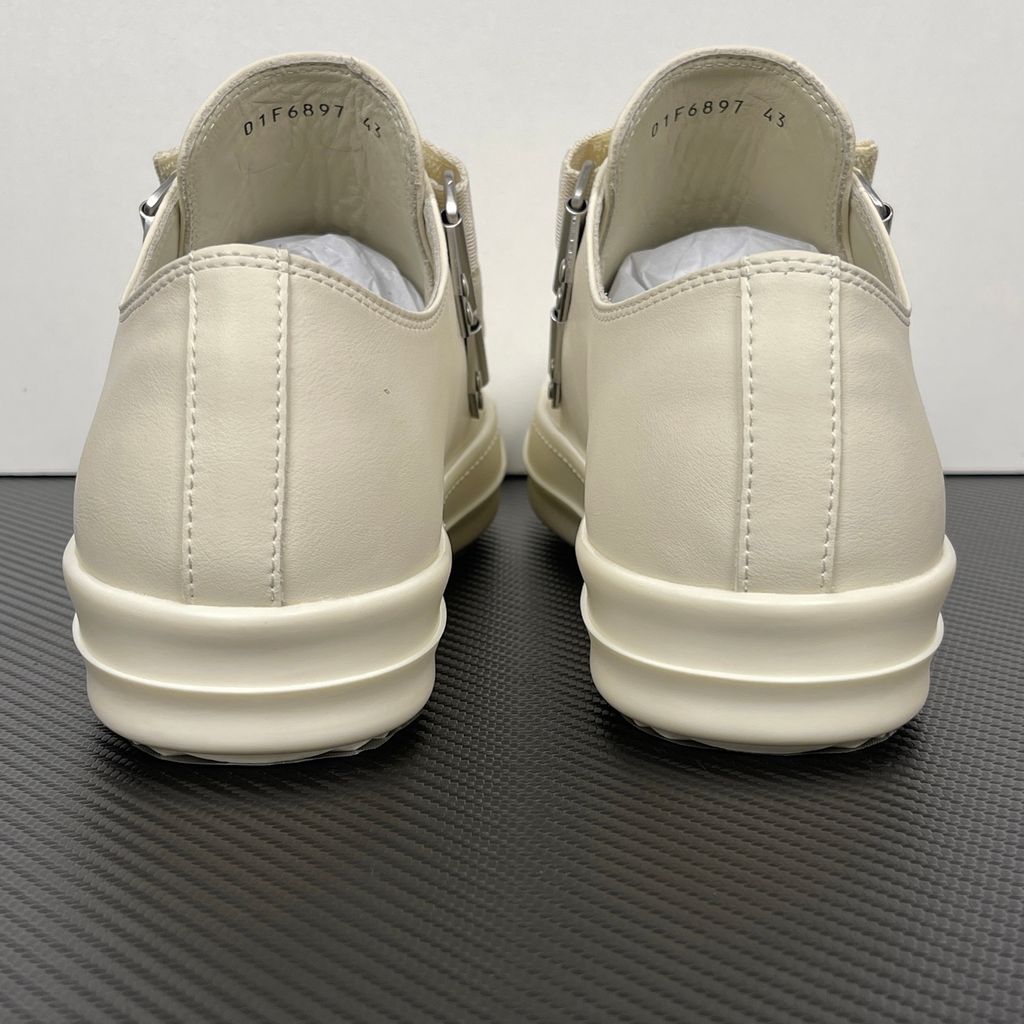 Side profile of the Rick Owens Mainline low-top sneaker in off-white leather, featuring distinctive industrial metal hardware, textured velcro strap closures, and a chunky tonal rubber sole.