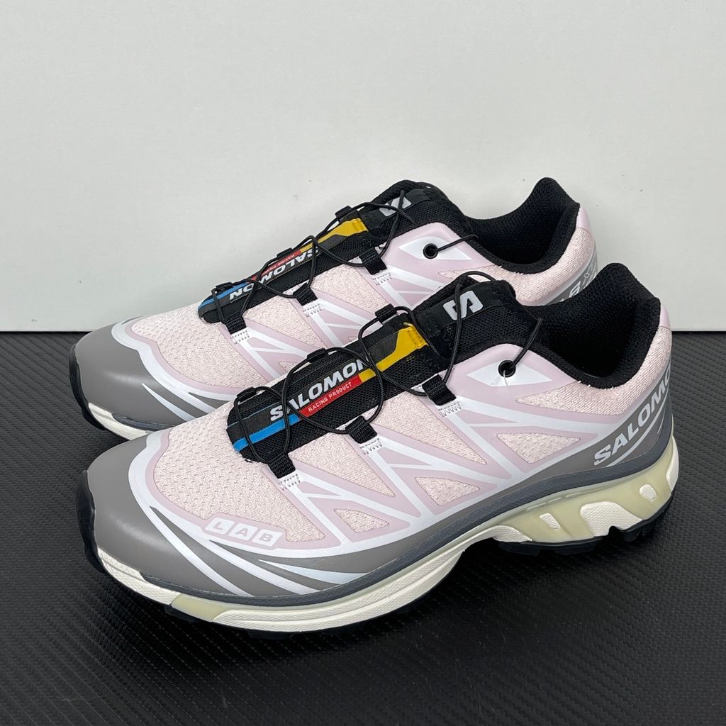 Side profile of the Salomon XT-6 trainers in a grey, white, and soft pink colorway, showcasing the technical mesh upper, "LAB" branding, and the cushioned ACS midsole.