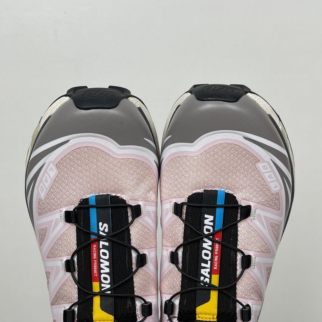 Side profile of the Salomon XT-6 trainers in a grey, white, and soft pink colorway, showcasing the technical mesh upper, "LAB" branding, and the cushioned ACS midsole.