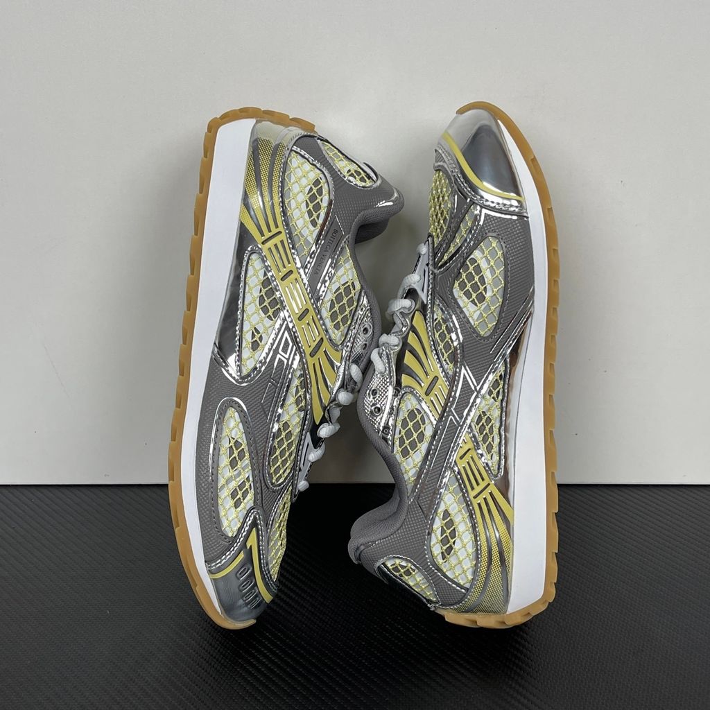 Side profile of the Bottega Veneta Orbit Runner sneaker, showcasing its intricate metallic and green-yellow technical mesh construction, prominent "BOTTEGA VENETA" branding, and the textured gum-tone outsole.