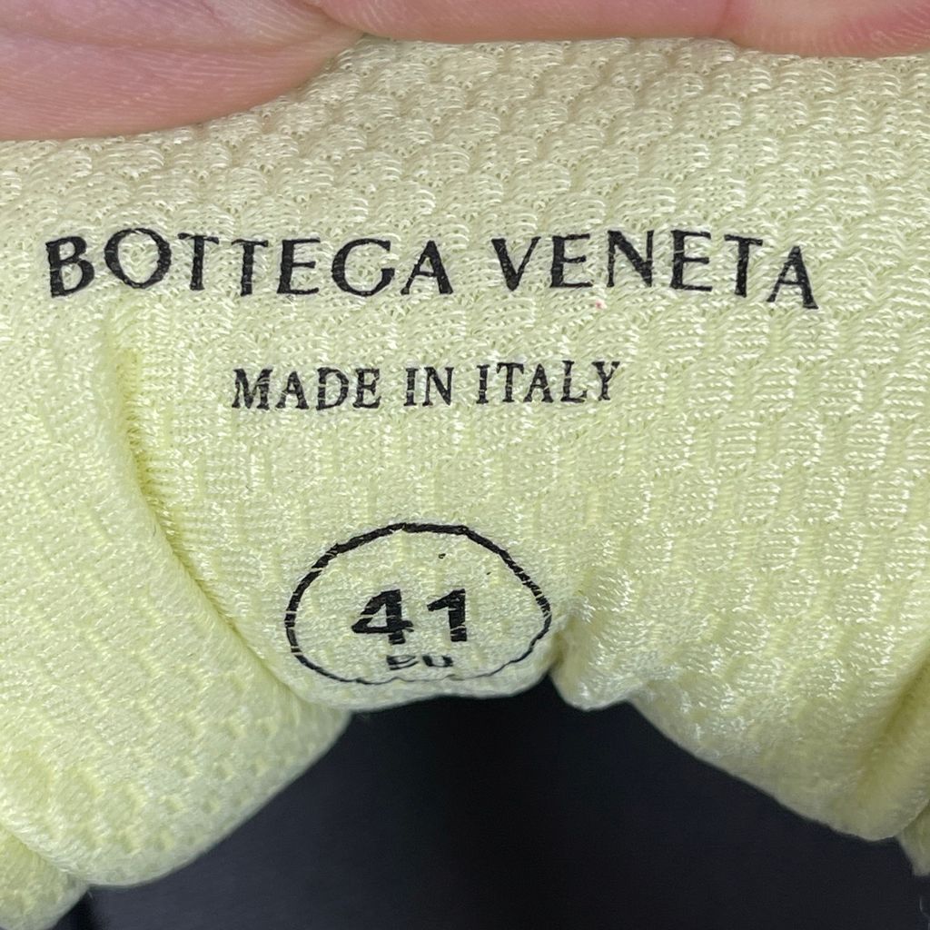 Side profile of the Bottega Veneta Orbit Runner sneaker, showcasing its intricate metallic and green-yellow technical mesh construction, prominent "BOTTEGA VENETA" branding, and the textured gum-tone outsole.