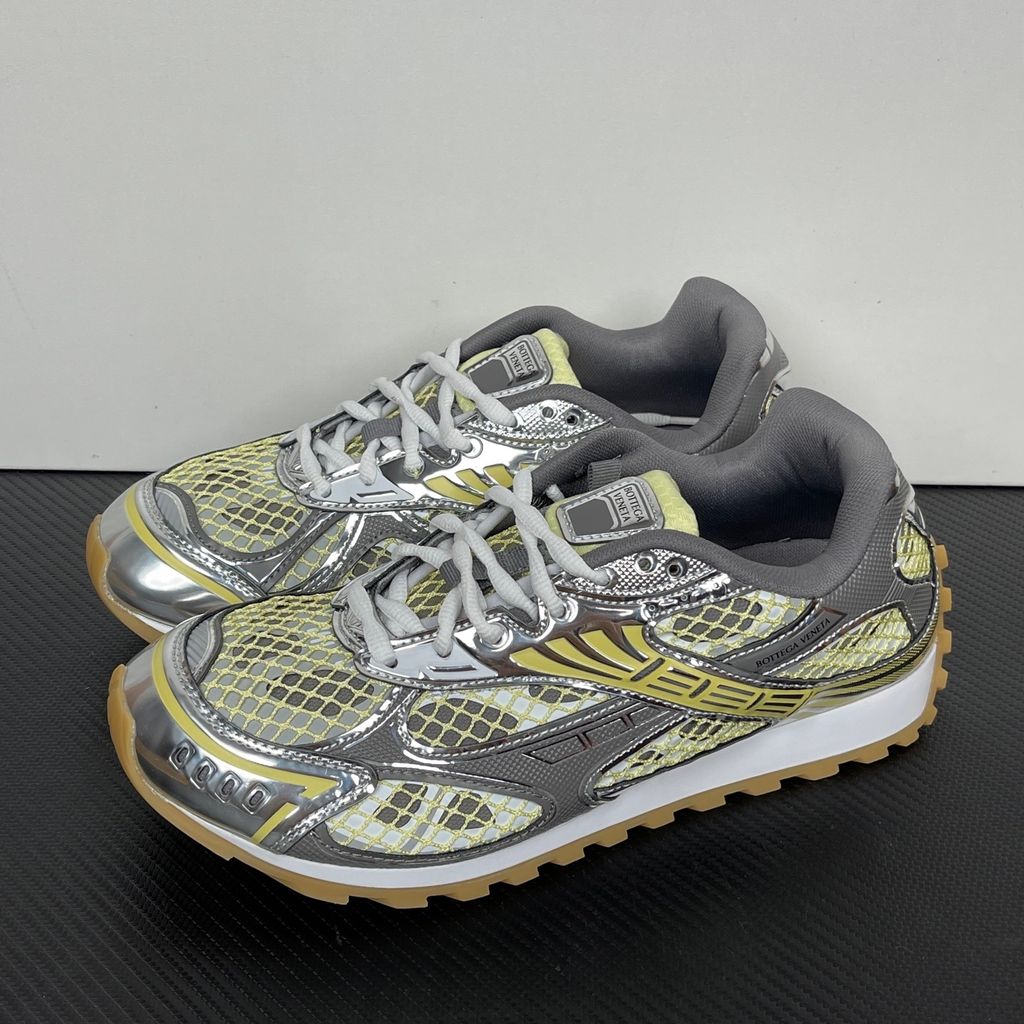 Side profile of the Bottega Veneta Orbit Runner sneaker, showcasing its intricate metallic and green-yellow technical mesh construction, prominent "BOTTEGA VENETA" branding, and the textured gum-tone outsole.