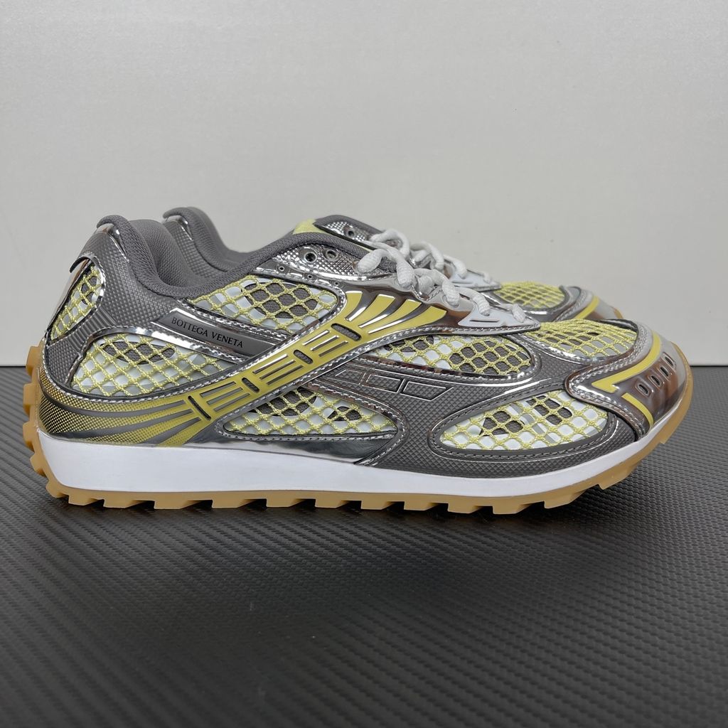 Side profile of the Bottega Veneta Orbit Runner sneaker, showcasing its intricate metallic and green-yellow technical mesh construction, prominent "BOTTEGA VENETA" branding, and the textured gum-tone outsole.