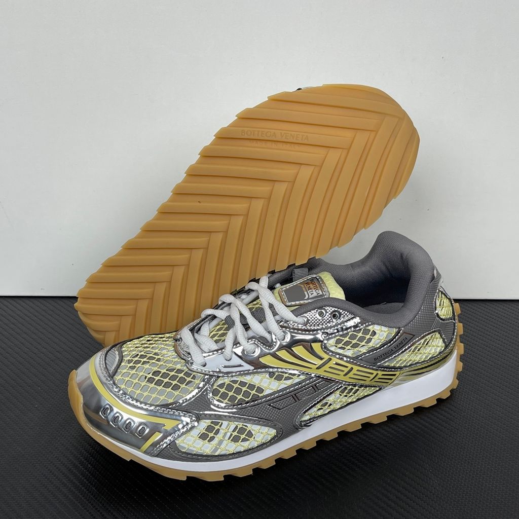 Side profile of the Bottega Veneta Orbit Runner sneaker, showcasing its intricate metallic and green-yellow technical mesh construction, prominent "BOTTEGA VENETA" branding, and the textured gum-tone outsole.