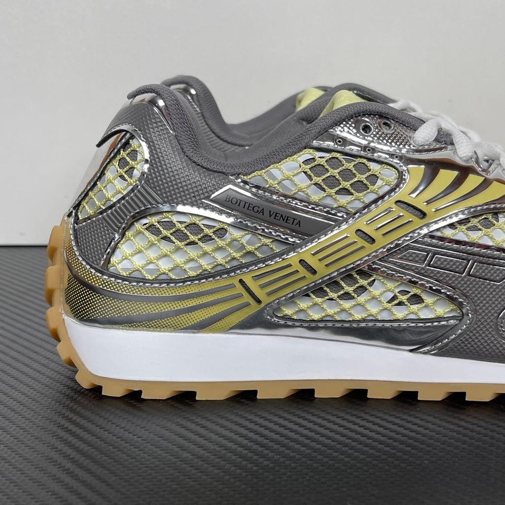 Side profile of the Bottega Veneta Orbit Runner sneaker, showcasing its intricate metallic and green-yellow technical mesh construction, prominent "BOTTEGA VENETA" branding, and the textured gum-tone outsole.