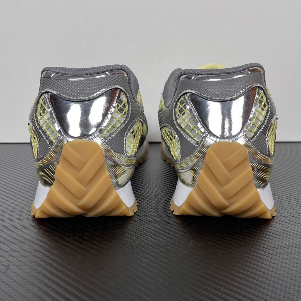 Side profile of the Bottega Veneta Orbit Runner sneaker, showcasing its intricate metallic and green-yellow technical mesh construction, prominent "BOTTEGA VENETA" branding, and the textured gum-tone outsole.