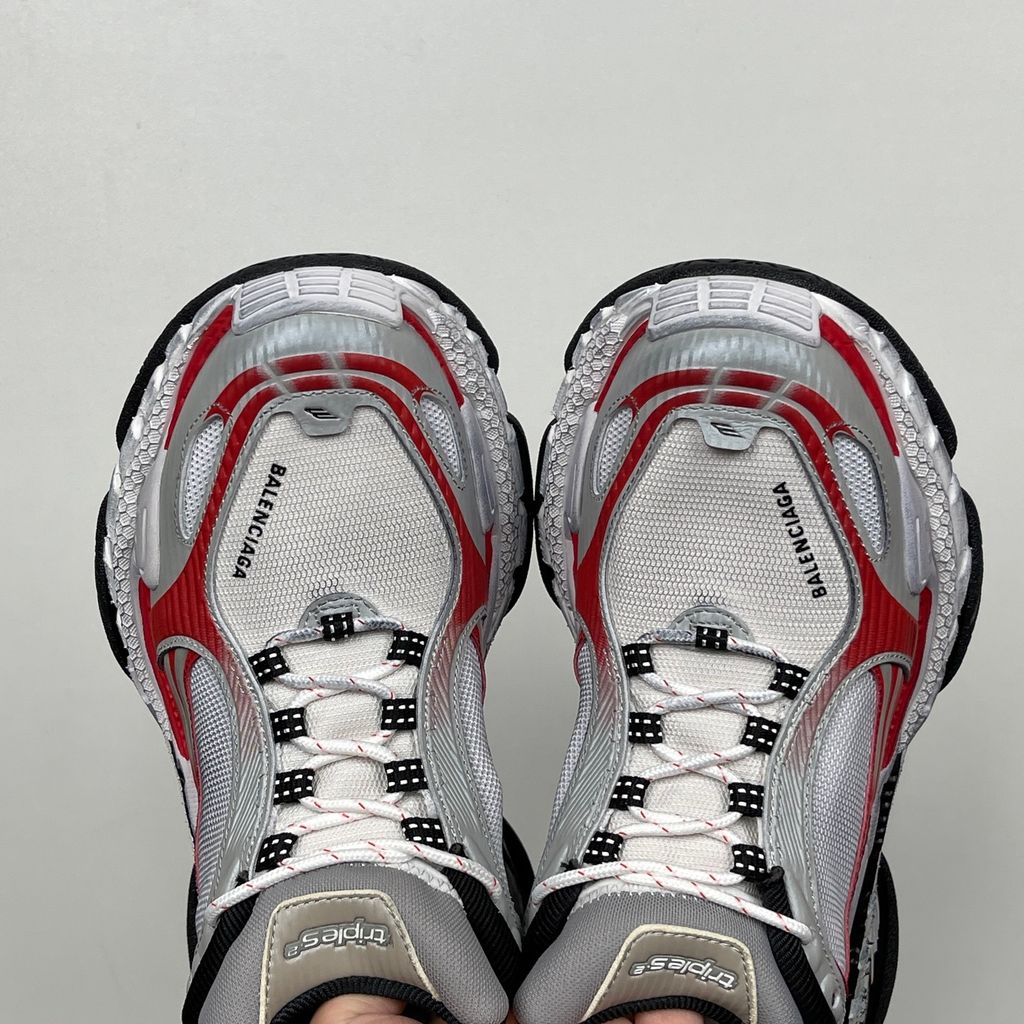 Side profile of the Balenciaga Triple S 2 sneaker, showcasing the complex layered mesh and synthetic upper in grey, red, and white, alongside the signature distressed chunky, multi-layered rubber sole.