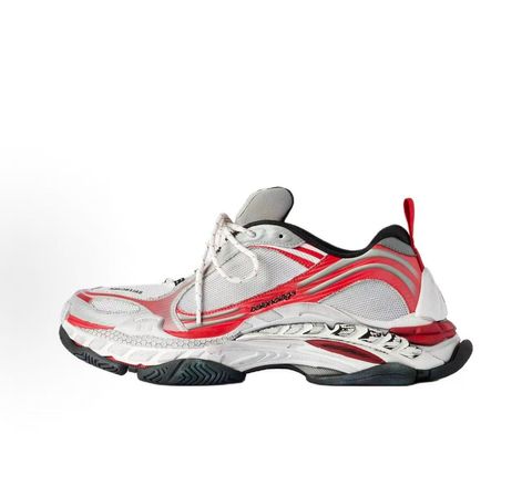 Side profile of the Balenciaga Triple S 2 sneaker, showcasing the complex layered mesh and synthetic upper in grey, red, and white, alongside the signature distressed chunky, multi-layered rubber sole.