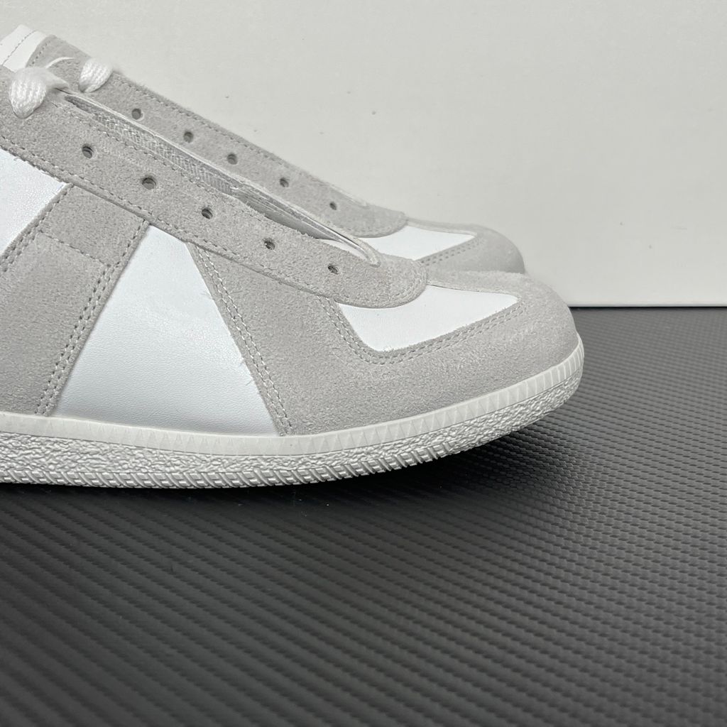 Side profile of the Maison Margiela Replica Low-Top sneakers in white, featuring a premium calfskin leather upper, tonal light grey suede overlays, and a textured white rubber sole.