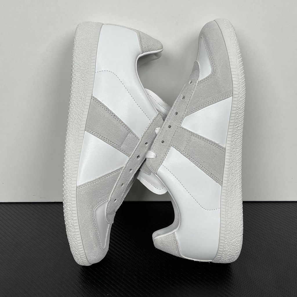 Side profile of the Maison Margiela Replica Low-Top sneakers in white, featuring a premium calfskin leather upper, tonal light grey suede overlays, and a textured white rubber sole.