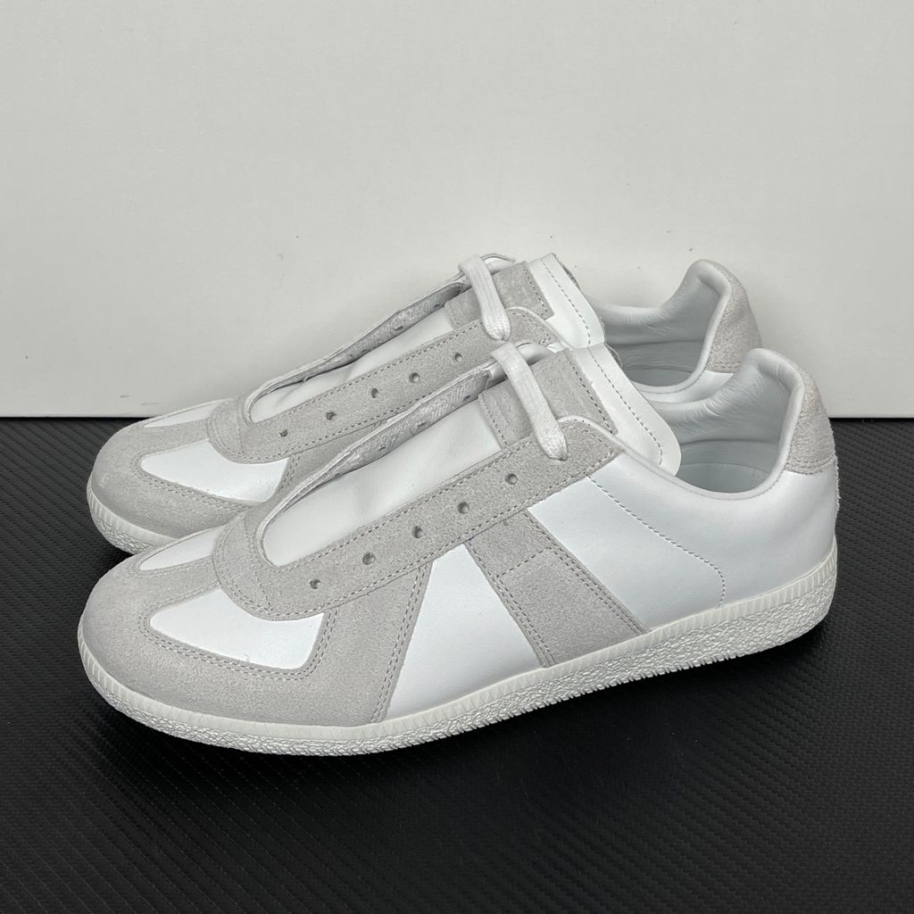Side profile of the Maison Margiela Replica Low-Top sneakers in white, featuring a premium calfskin leather upper, tonal light grey suede overlays, and a textured white rubber sole.