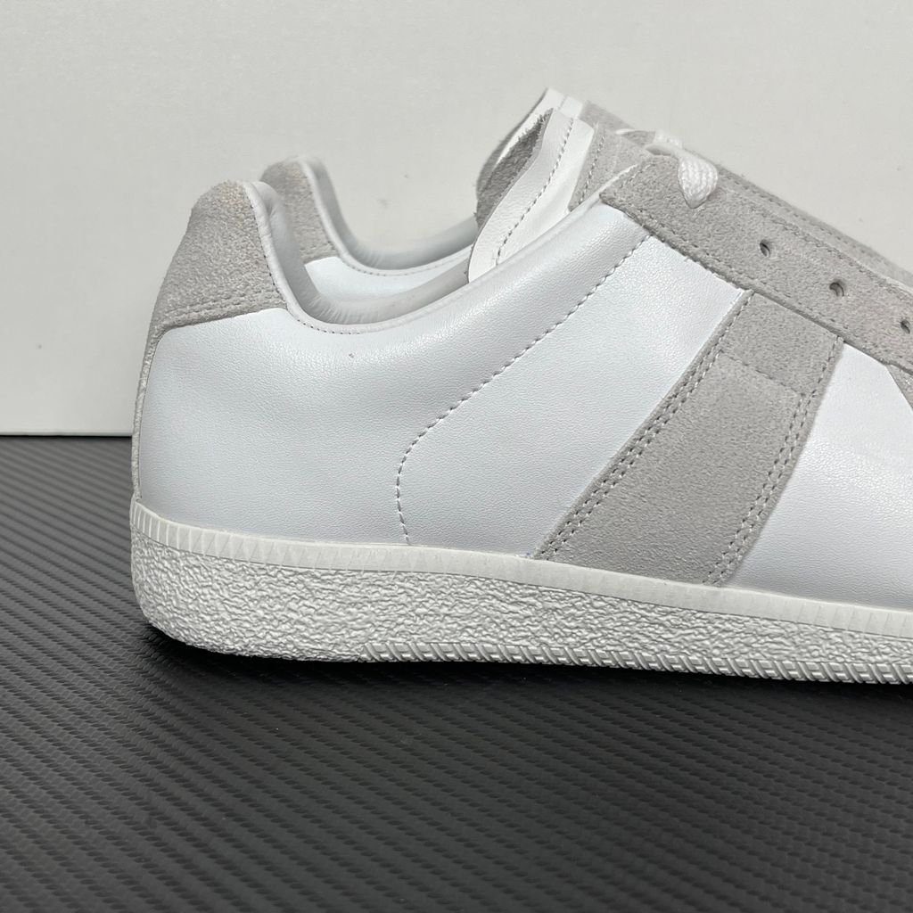 Side profile of the Maison Margiela Replica Low-Top sneakers in white, featuring a premium calfskin leather upper, tonal light grey suede overlays, and a textured white rubber sole.