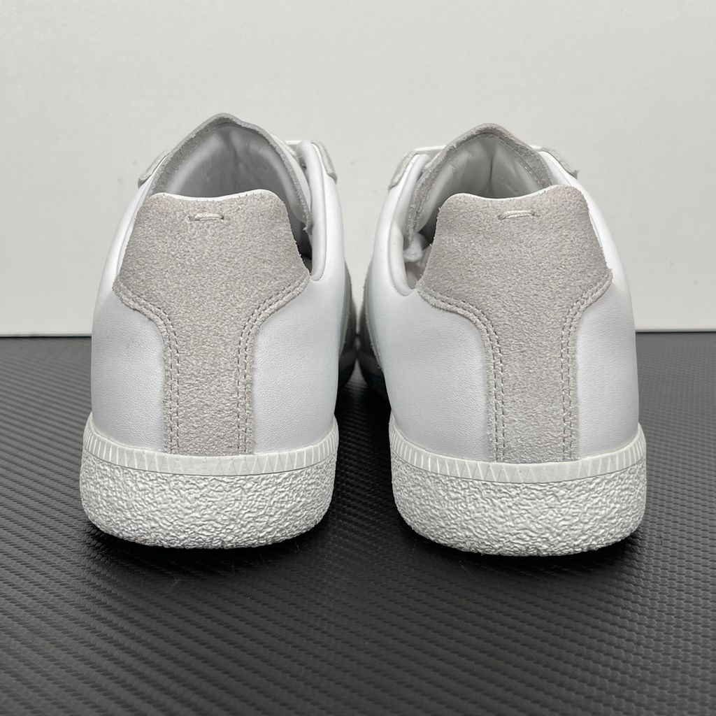 Side profile of the Maison Margiela Replica Low-Top sneakers in white, featuring a premium calfskin leather upper, tonal light grey suede overlays, and a textured white rubber sole.