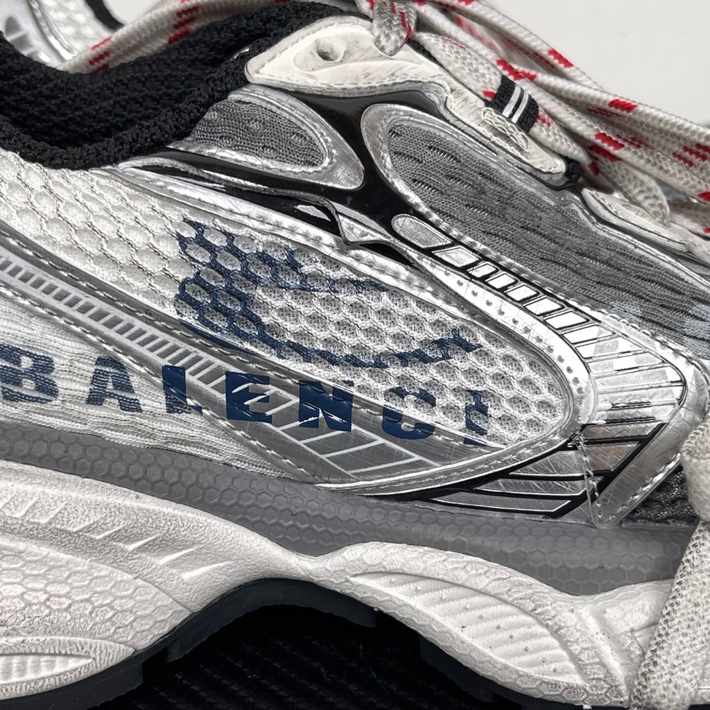 Side profile of the Balenciaga 3XL Sneakers in a distressed silver and white colorway, showcasing the complex metallic overlays, wide mesh base, exaggerated chunky runner sole, and the signature extra laces wrapped around the toe box.
