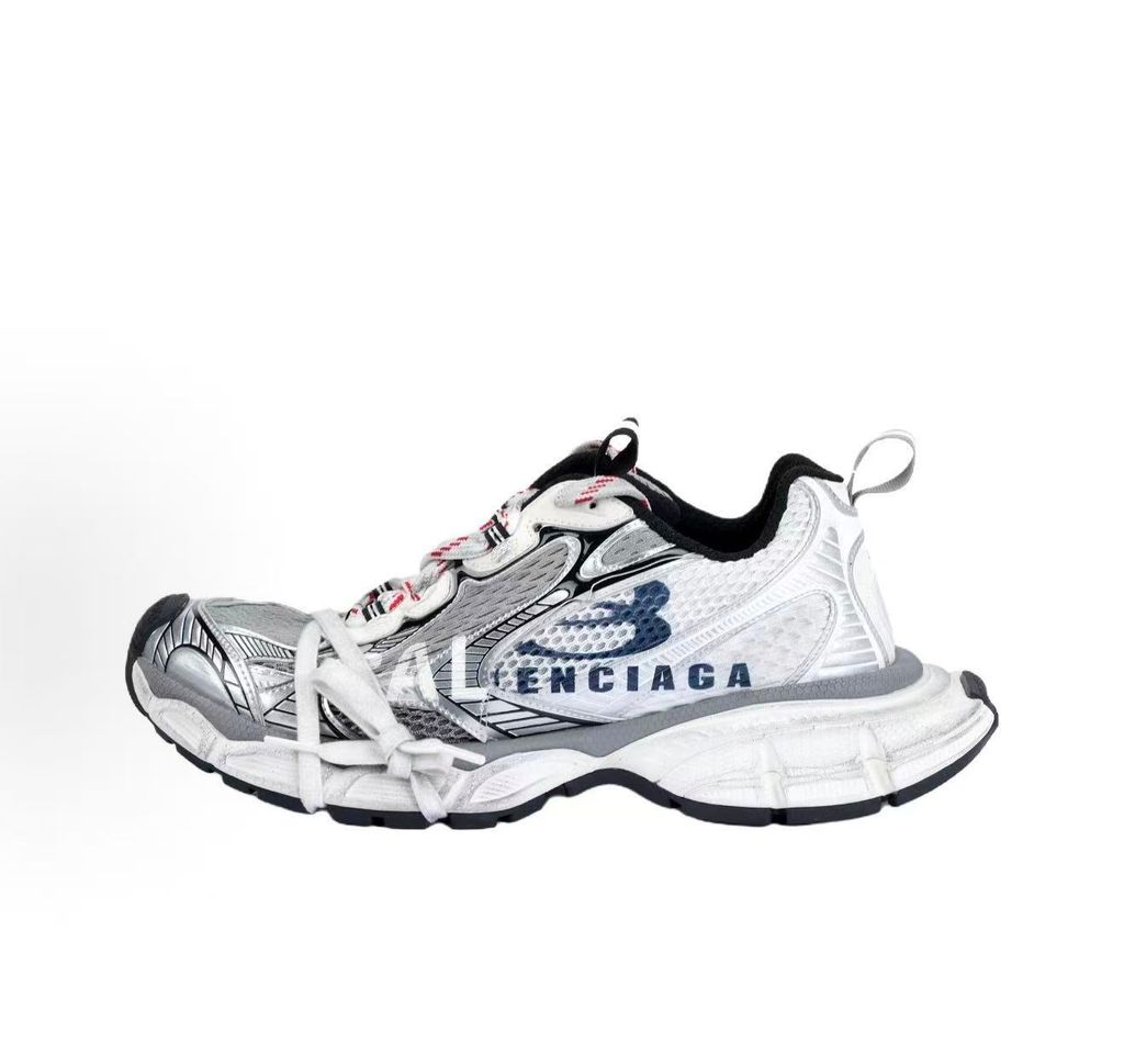 Side profile of the Balenciaga 3XL Sneakers in a distressed silver and white colorway, showcasing the complex metallic overlays, wide mesh base, exaggerated chunky runner sole, and the signature extra laces wrapped around the toe box.