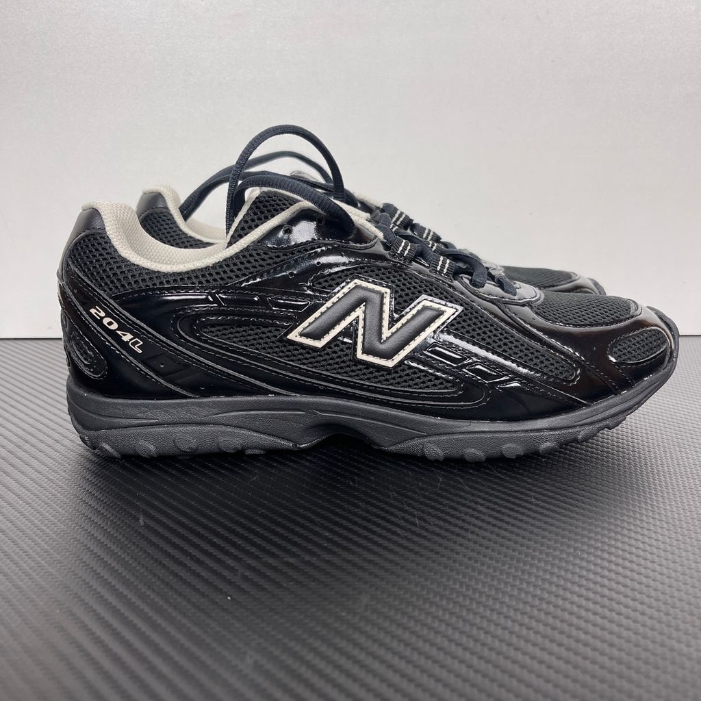 Side profile of the New Balance 204L 'Black Timberwolf', showcasing the breathable black mesh upper, dynamic taupe-grey Timberwolf synthetic overlays, classic 'N' logo, and a sleek, cushioned runner midsole.