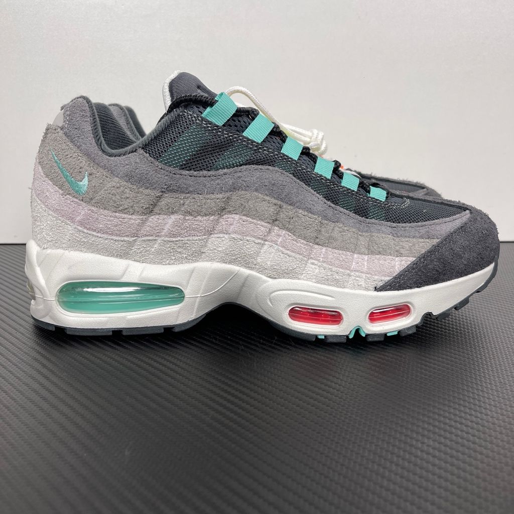 Side profiles of the left and right Nike Air Max 95 OG 'Big Bubble' Greedy (2026) sneakers, showcasing the asymmetrical, mismatched multi-color gradient uppers and the exaggerated visible Air units in the black midsole.