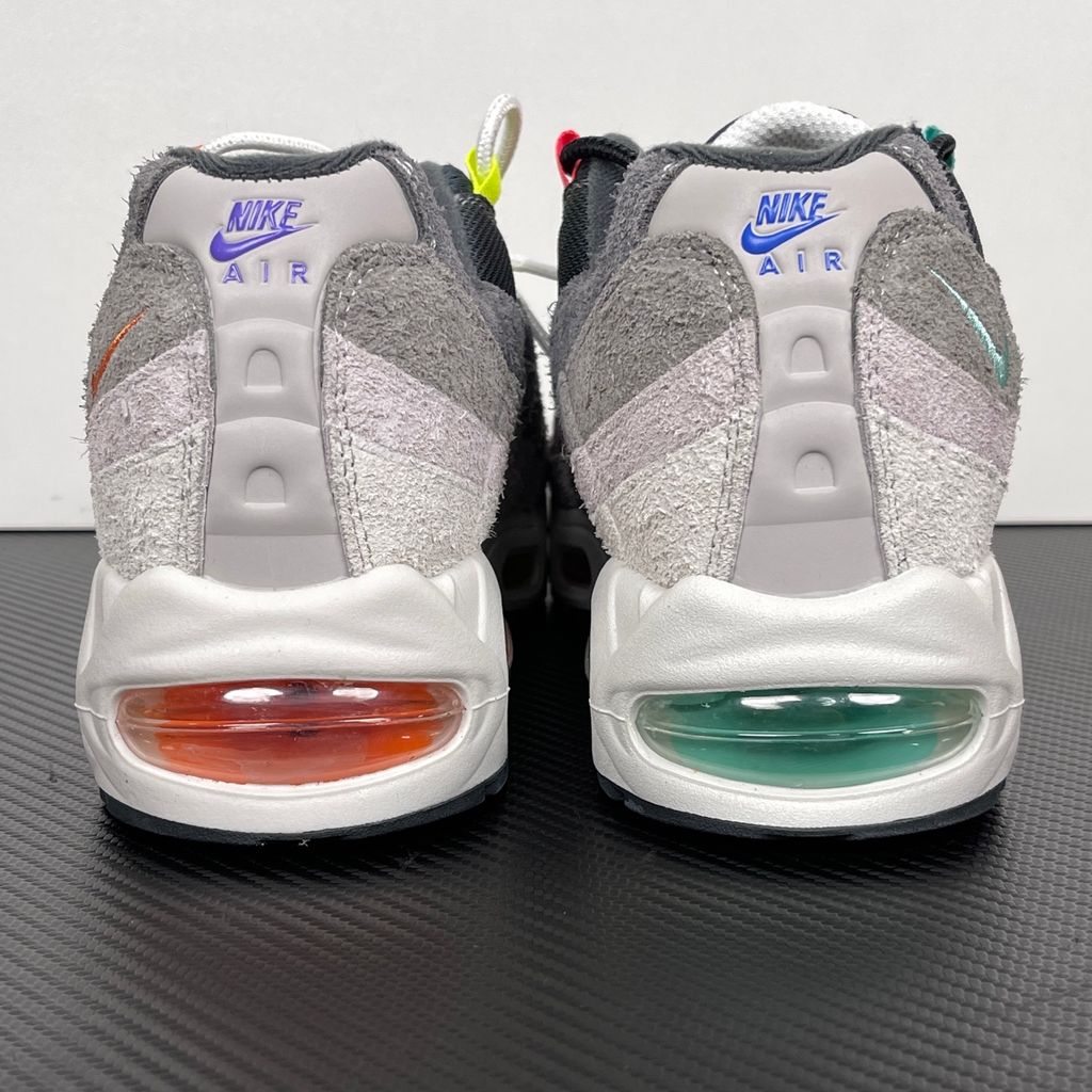 Side profiles of the left and right Nike Air Max 95 OG 'Big Bubble' Greedy (2026) sneakers, showcasing the asymmetrical, mismatched multi-color gradient uppers and the exaggerated visible Air units in the black midsole.