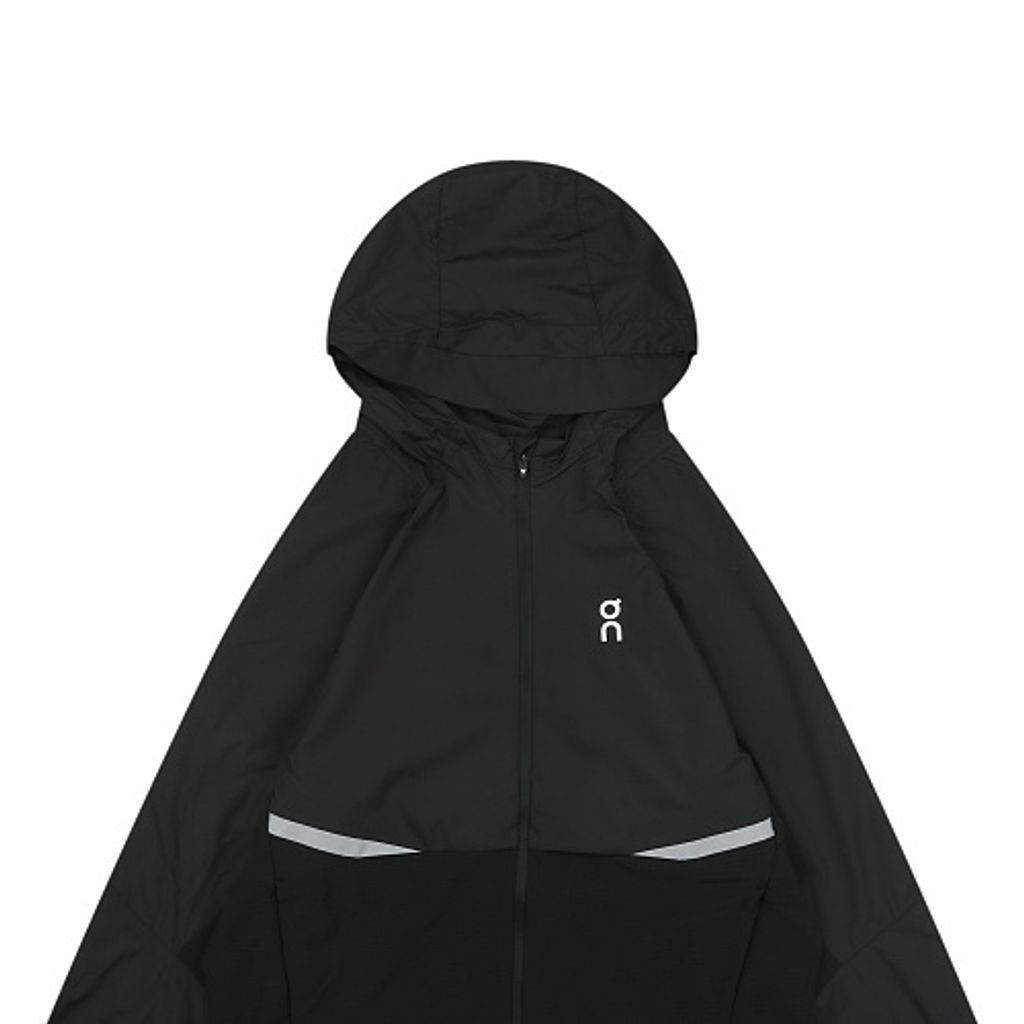 Front profile of the men's On Running Core Jacket in black, showcasing the lightweight windproof fabric, full-length front zipper, protective hood, white 'On' logo, and sleek reflective strips across the midsection for night safety.