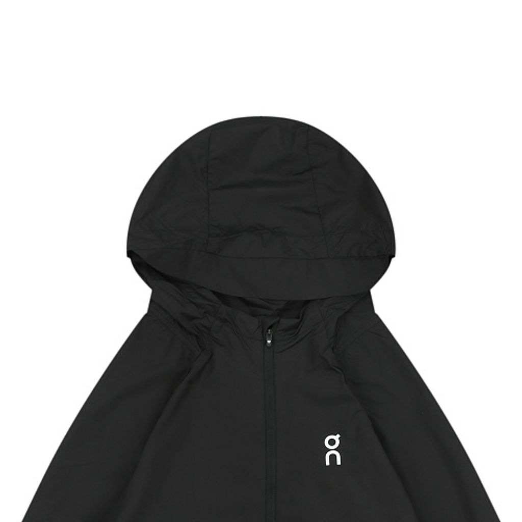 Front profile of the men's On Running Core Jacket in black, showcasing the lightweight windproof fabric, full-length front zipper, protective hood, white 'On' logo, and sleek reflective strips across the midsection for night safety.