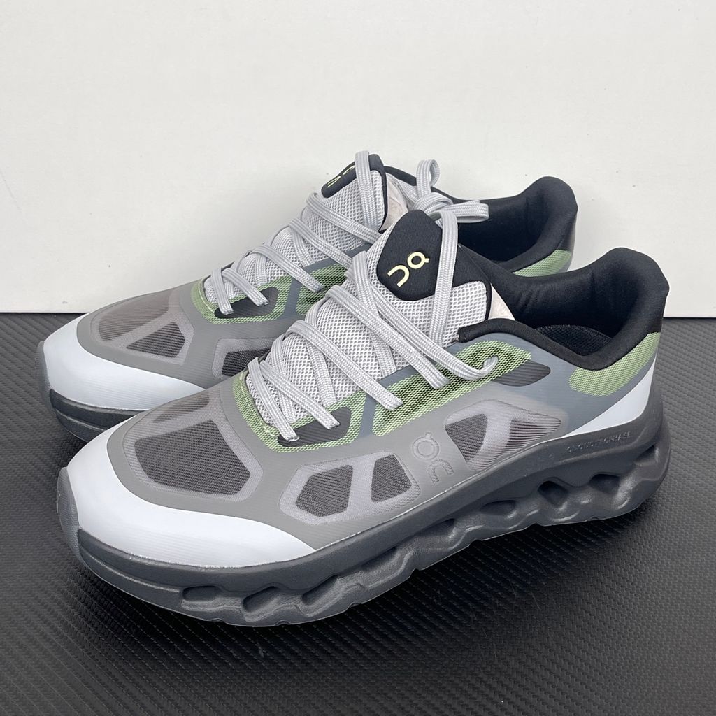 Side profile of the On Running Cloudtilt Remix sneaker, showcasing the mixed-material upper in dark grey and white with subtle green mesh undertones, quick-adjust speed lacing, and the distinctive dark grey CloudTec Phase® collapsing midsole.