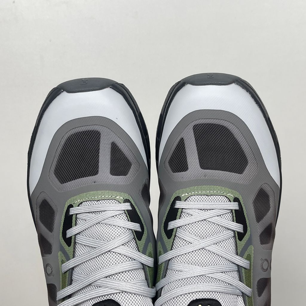 Side profile of the On Running Cloudtilt Remix sneaker, showcasing the mixed-material upper in dark grey and white with subtle green mesh undertones, quick-adjust speed lacing, and the distinctive dark grey CloudTec Phase® collapsing midsole.
