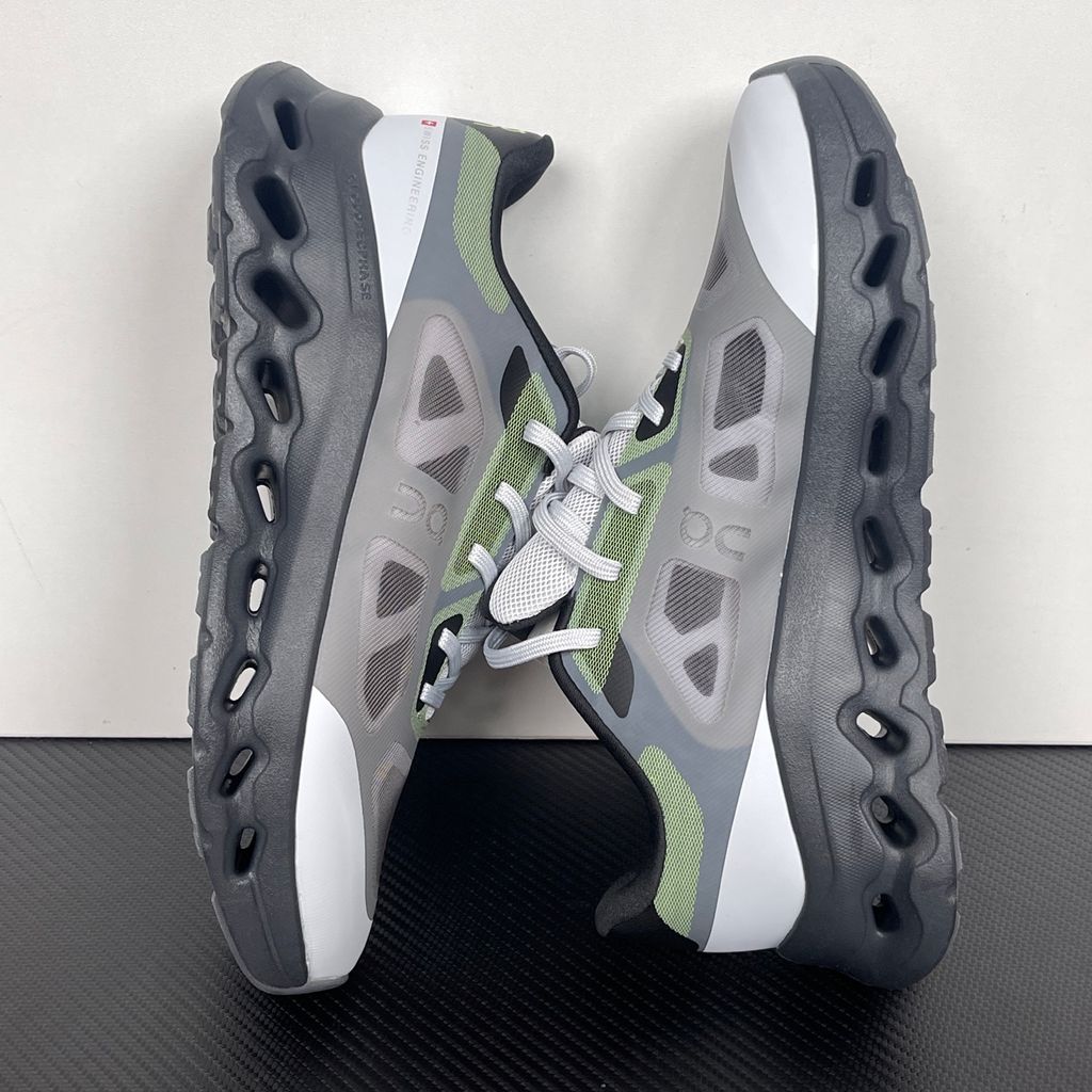 Side profile of the On Running Cloudtilt Remix sneaker, showcasing the mixed-material upper in dark grey and white with subtle green mesh undertones, quick-adjust speed lacing, and the distinctive dark grey CloudTec Phase® collapsing midsole.