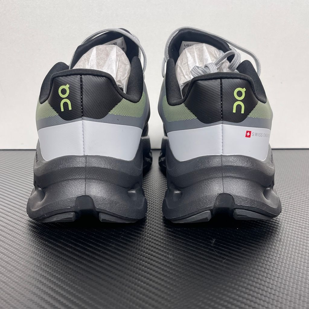 Side profile of the On Running Cloudtilt Remix sneaker, showcasing the mixed-material upper in dark grey and white with subtle green mesh undertones, quick-adjust speed lacing, and the distinctive dark grey CloudTec Phase® collapsing midsole.